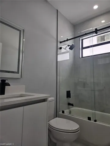 Bathroom with toilet, vanity, and enclosed tub / shower combo