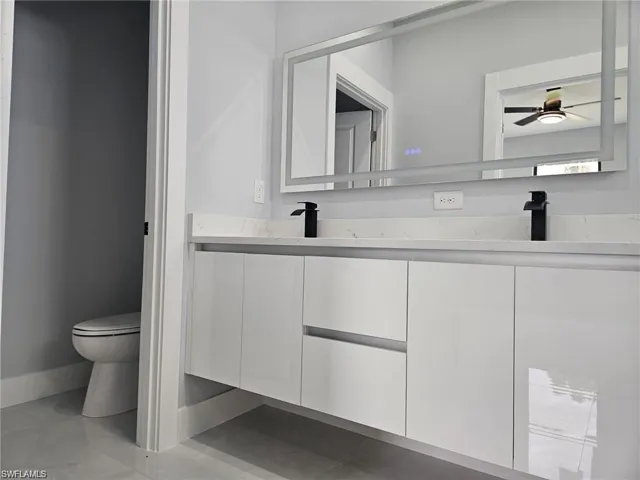 Full bathroom with double vanity, toilet, ceiling fan, and baseboards