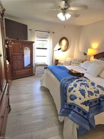 Bedroom with a textured ceiling, light hardwood / wood-style flooring, and ceiling fan