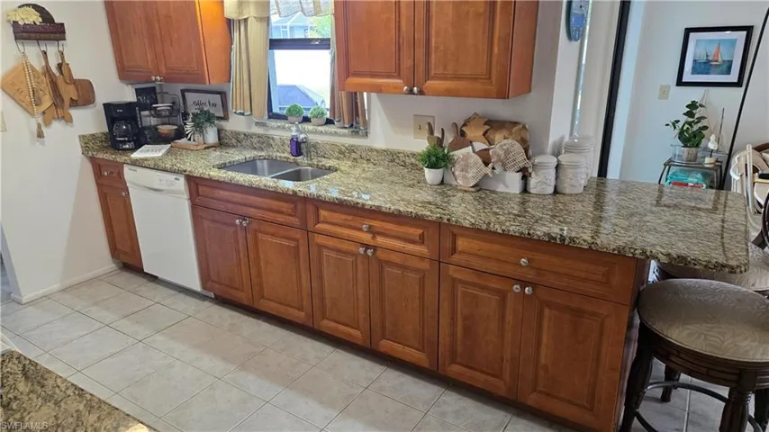 Kitchen with dishwasher, sink, a kitchen breakfast bar, light stone counters, and light tile patterned floors