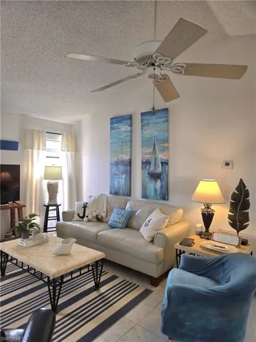 Living room with lofted ceiling, light tile patterned floors, a textured ceiling, and ceiling fan