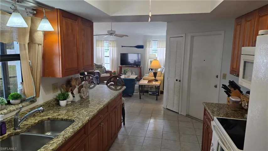 Kitchen with light stone countertops, white appliances, ceiling fan, sink, and pendant lighting