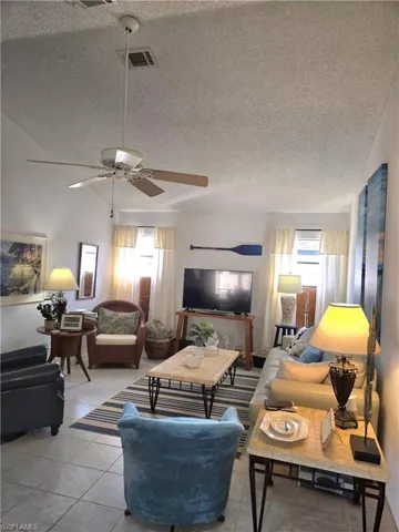 Tiled living room with plenty of natural light, a textured ceiling, lofted ceiling, and ceiling fan