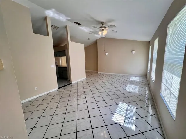 Empty room featuring lofted ceiling, a ceiling fan, and light tile patterned floors