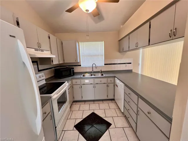Kitchen featuring white appliances, gray cabinetry, tasteful backsplash, light tile patterned floors, and dark countertops
