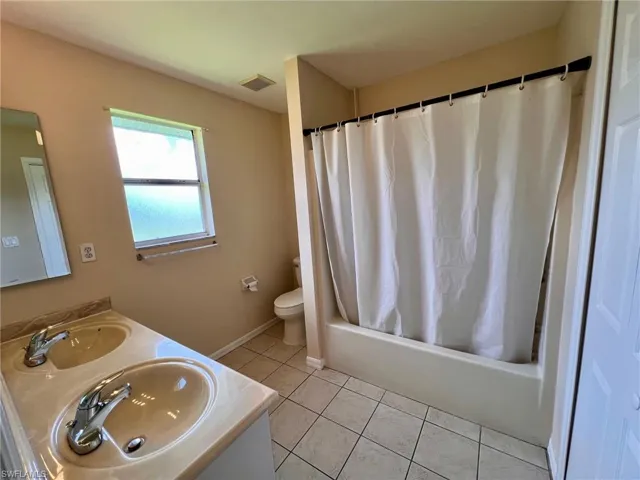 Bathroom with shower / bath combination with curtain, light tile patterned floors, and double vanity