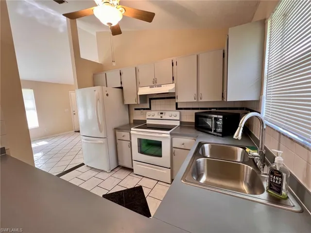 Kitchen featuring light tile patterned floors, white appliances, tasteful backsplash, ceiling fan, and high vaulted ceiling