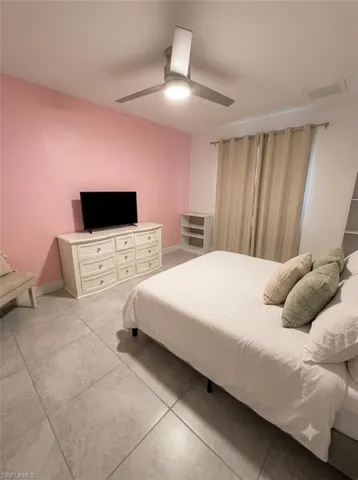 Bedroom featuring a modern ceiling fan with integrated lighting, tiled flooring, and a window with neutral drapes