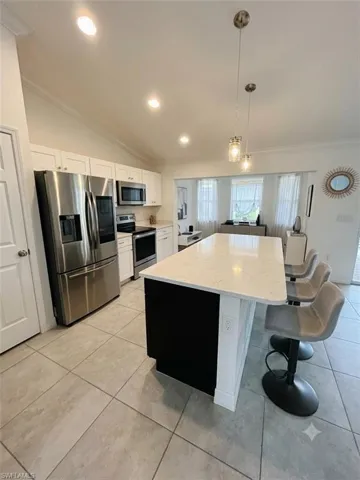 Modern kitchen featuring a large central island with seating, stainless steel appliances, white cabinetry, vaulted ceilings, and recessed lighting