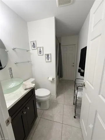 Efficient full bathroom featuring a dark vanity with integrated sink, ceramic tile flooring, toilet, and framed mirror