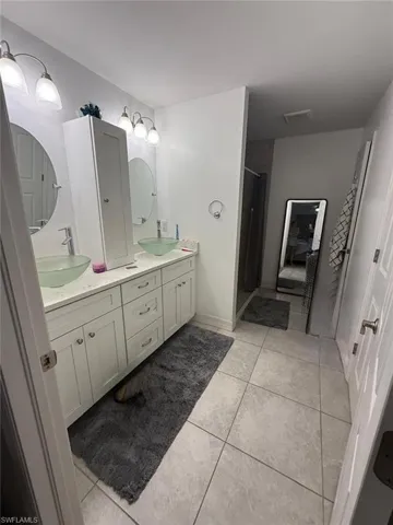Spacious primary bathroom featuring dual vanity with ample storage cabinetry, ceramic tile flooring, sconce lighting, and generous countertop space