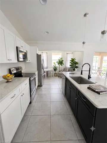 Galley kitchen featuring white cabinetry with hardware accents, stainless steel appliances including a built-in microwave, quartz countertops, a large island with contrasting black cabinetry and undermount sink with pull-down faucet, and tile flooring throughout