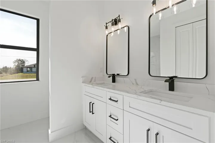 Bathroom featuring baseboards, a sink, marble finish floor, and double vanity