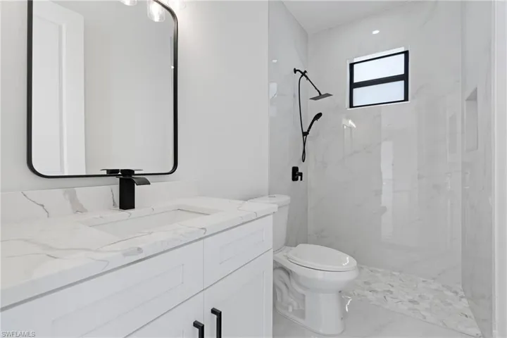 Bathroom featuring vanity, marble finish floor, a marble finish shower, and toilet