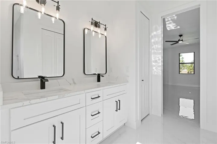 Bathroom featuring ceiling fan, a sink, double vanity, marble finish floor, and baseboards