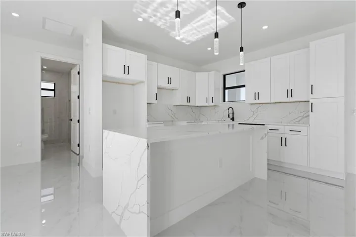 Kitchen with light stone countertops, marble finish floor, white cabinetry, backsplash, and a kitchen island