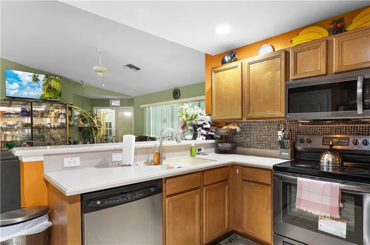 Kitchen with stainless steel appliances, a peninsula, light countertops, decorative backsplash, and lofted ceiling
