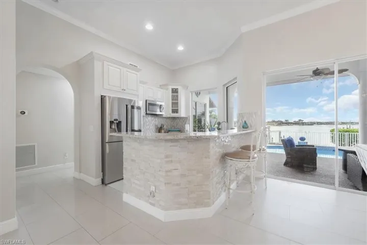 Kitchen featuring glass insert cabinets, tasteful backsplash, stainless steel appliances, white cabinets, and light stone counters