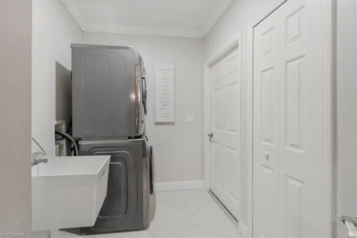 Laundry room featuring ornamental molding, stacked washer / drying machine, and light tile patterned flooring