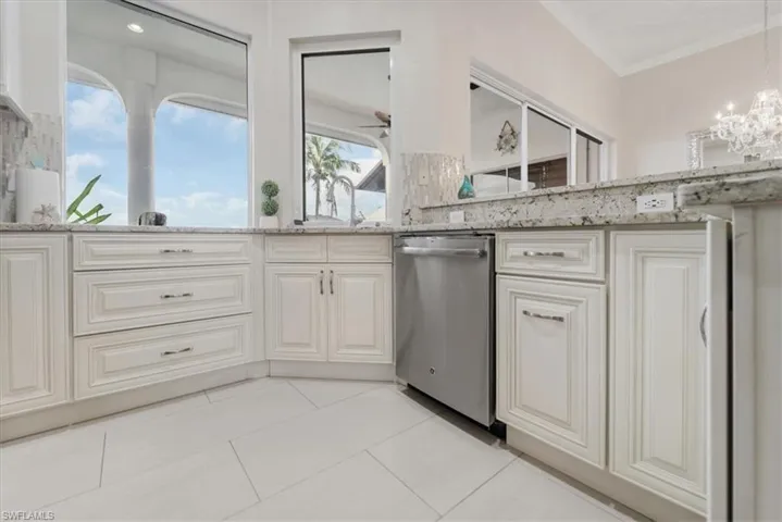Kitchen with light tile patterned floors, light stone counters, dishwasher, a chandelier, and decorative light fixtures