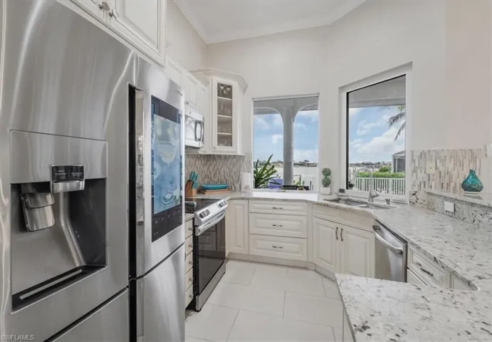 Kitchen featuring appliances with stainless steel finishes, light stone countertops, glass insert cabinets, tasteful backsplash, and crown molding