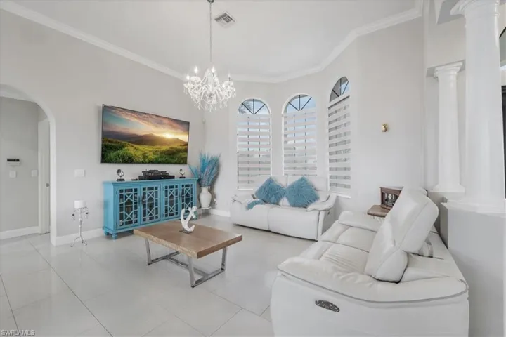 Living area with arched walkways, ornamental molding, tile patterned floors, and a chandelier