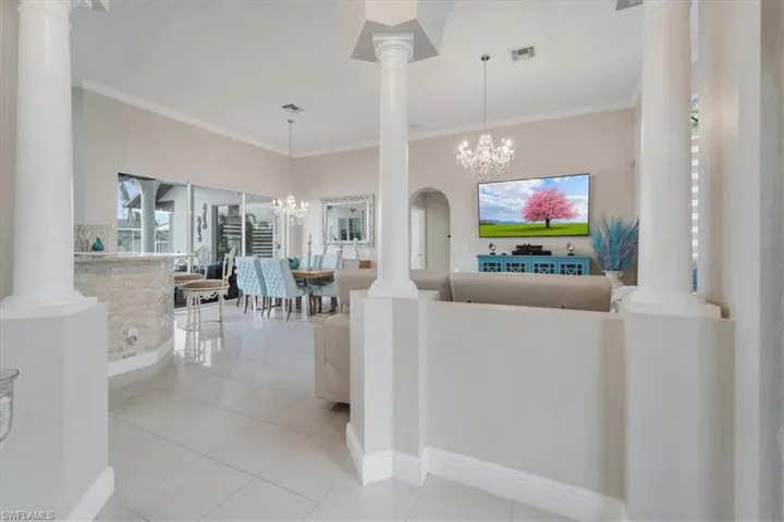 Living area featuring crown molding, ornate columns, a chandelier, and light tile patterned flooring