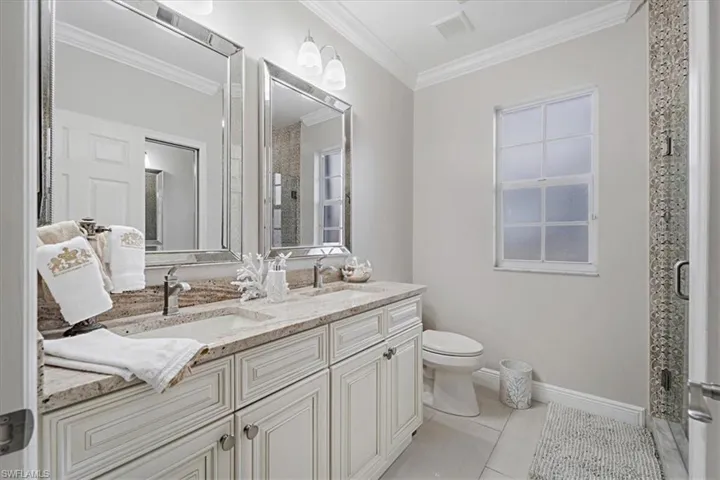 Bathroom featuring a shower stall, double vanity, light tile patterned floors, and crown molding