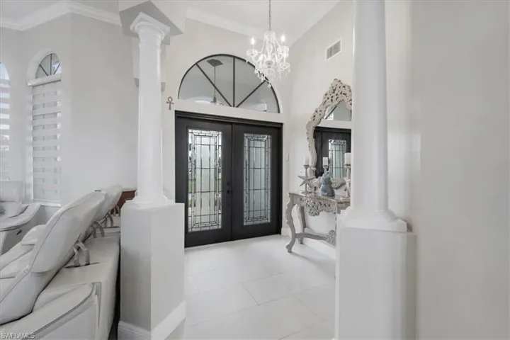 Tiled foyer entrance with decorative columns, french doors, ornamental molding, a chandelier, and a high ceiling