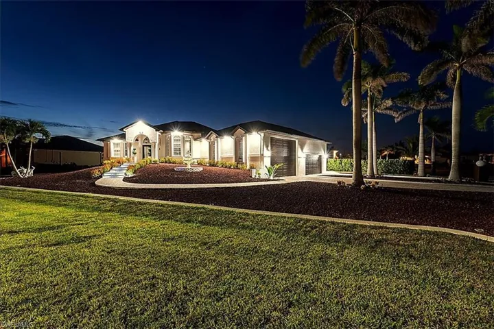 Back of house at twilight featuring stucco siding, driveway, a lawn, and an attached garage