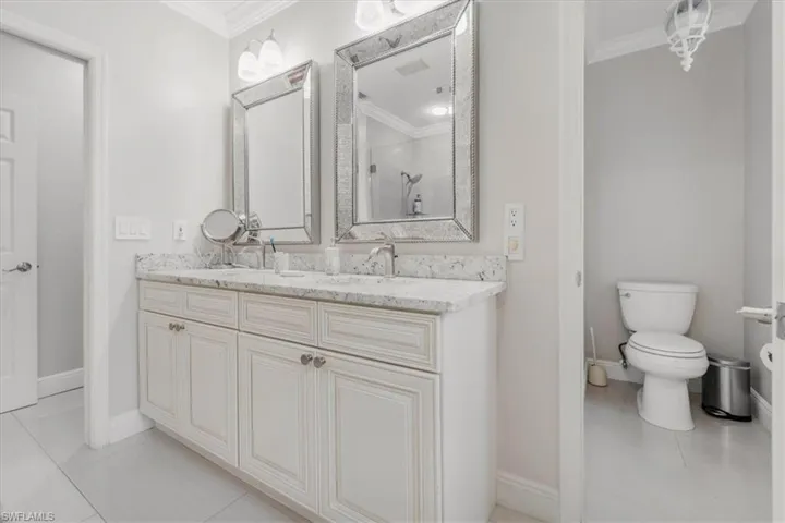 Full bath featuring light tile patterned flooring, ornamental molding, double vanity, and a stall shower