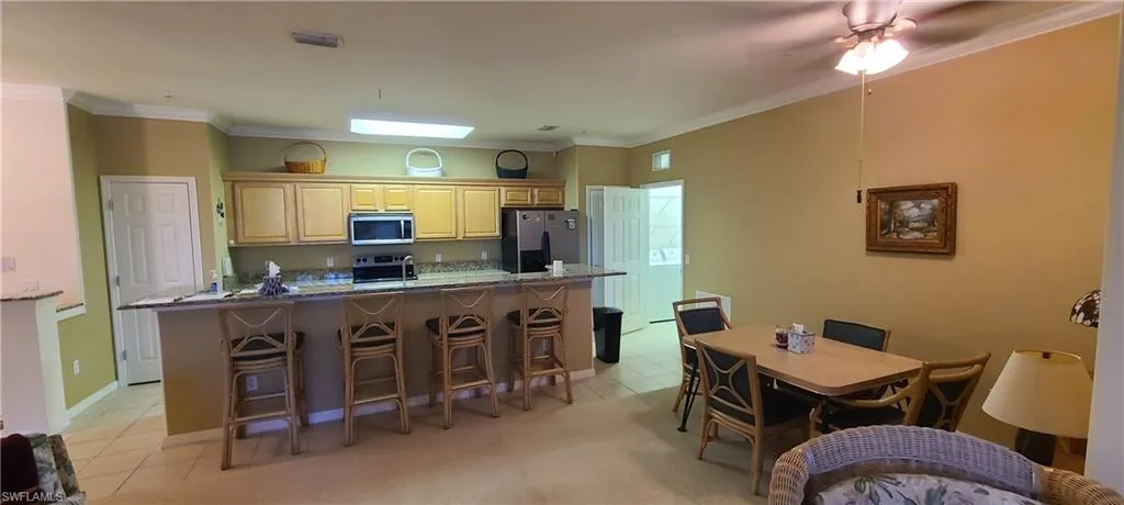 Kitchen featuring light tile patterned flooring, ornamental molding, stainless steel appliances, dark stone counters, and light brown cabinets