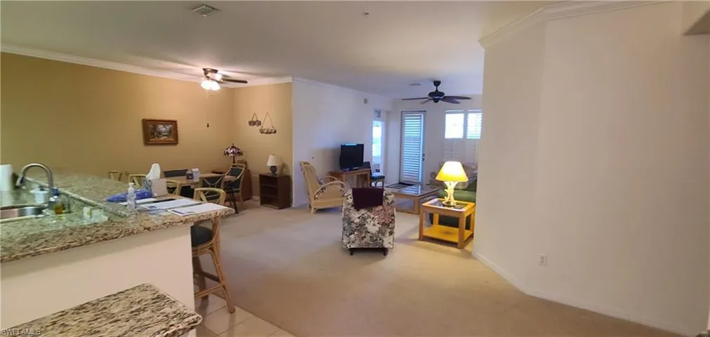 Living area with light carpet, ornamental molding, and light tile patterned flooring