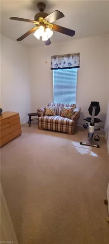Carpeted living area featuring a ceiling fan and baseboards