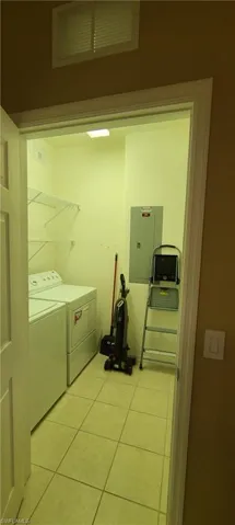 Laundry room featuring light tile patterned floors, electric panel, and washer and dryer