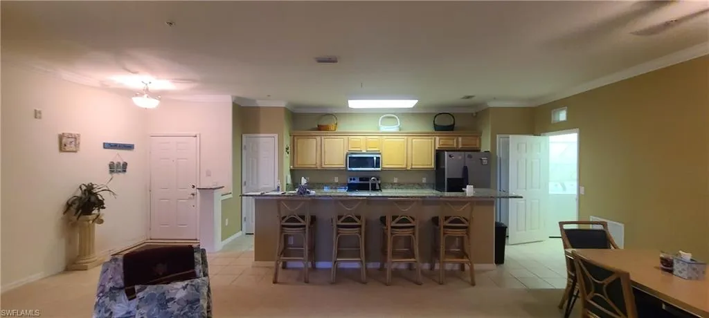Kitchen with stainless steel appliances, a kitchen breakfast bar, light tile patterned floors, ornamental molding, and a kitchen island with sink