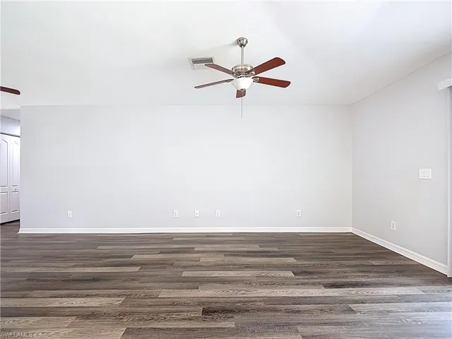 Empty room with a ceiling fan and dark wood-style flooring