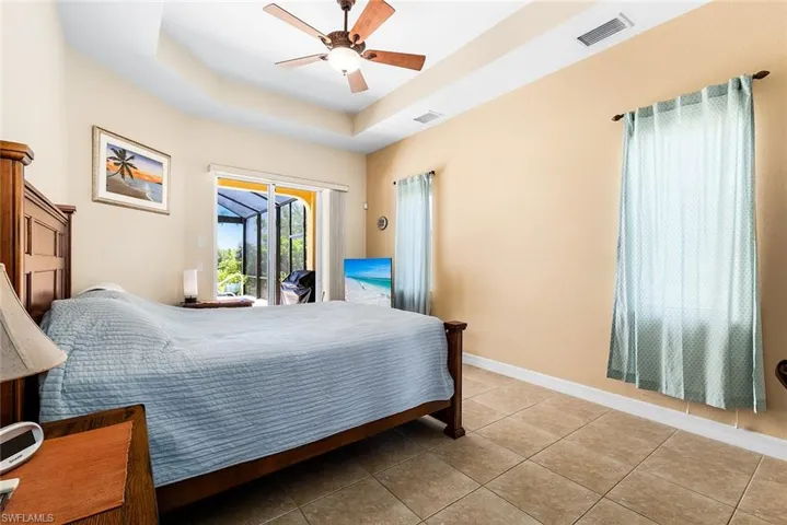 Tiled bedroom featuring a raised ceiling, ceiling fan, and access to exterior