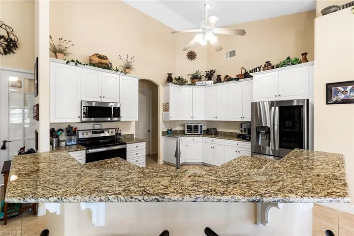 Kitchen with ceiling fan, stainless steel appliances, light tile floors, high vaulted ceiling, and a breakfast bar area