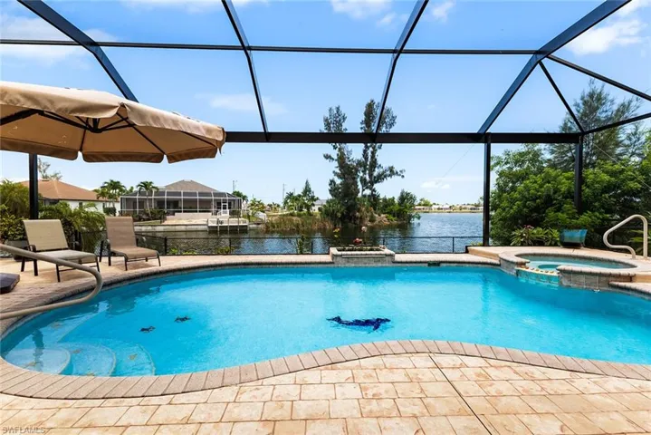 View of swimming pool with a patio, glass enclosure, an in ground hot tub, and a water view