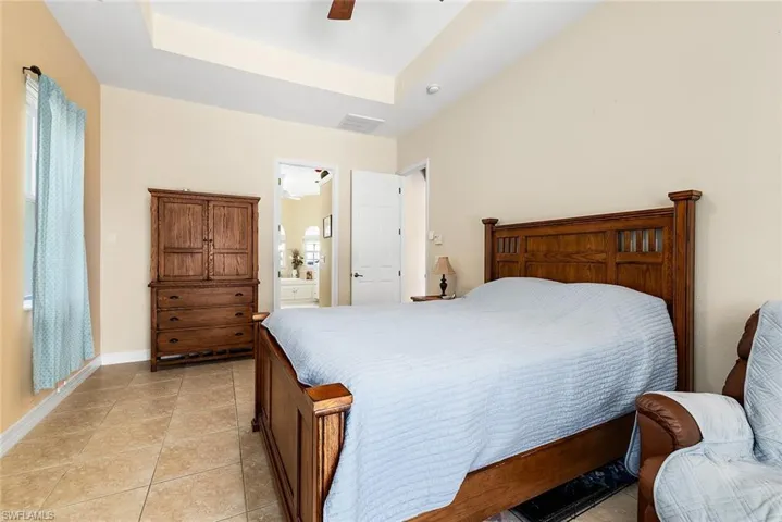 Tiled bedroom featuring connected bathroom, a raised ceiling, and ceiling fan