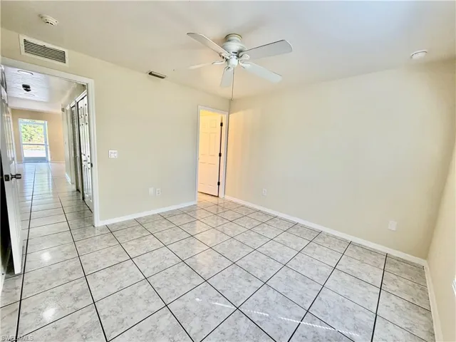 Empty room featuring a ceiling fan, light tile patterned flooring, and a smoke detector