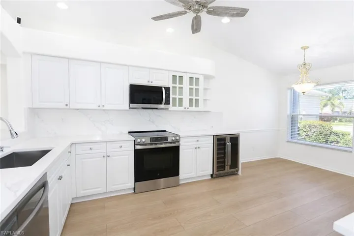 Kitchen with white cabinets, stainless steel appliances, decorative backsplash, wine cooler, and vaulted ceiling