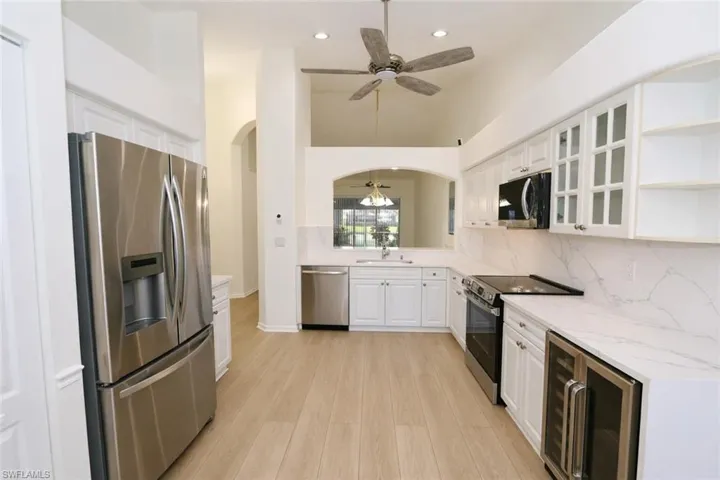 Kitchen featuring a ceiling fan, stainless steel appliances, open shelves, glass fronted cabinets, and wine cooler