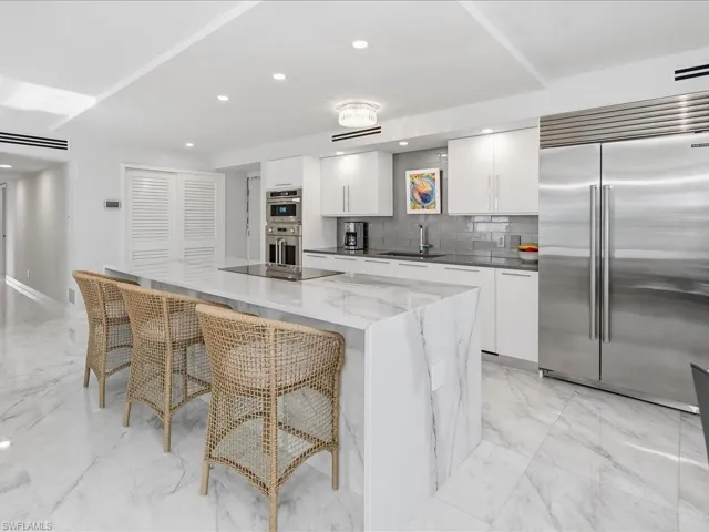 Kitchen with white cabinetry, appliances with stainless steel finishes, recessed lighting, light marble finish floors, and a kitchen bar