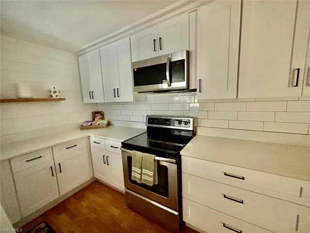Kitchen with appliances with stainless steel finishes, white cabinets, dark wood-type flooring, decorative backsplash, and open shelves