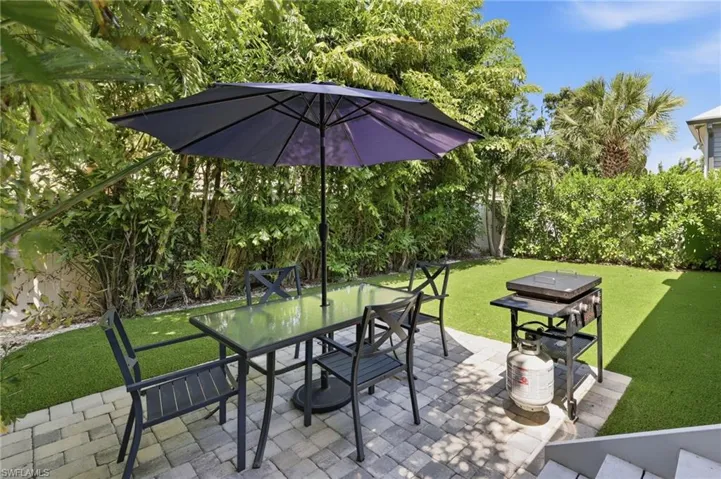 Outdoor entertaining space featuring a paver patio, lush perimeter plantings, and artificial turf lawn
