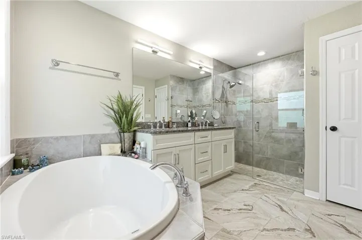 Spacious bathroom featuring a built-in soaking tub, a frameless glass shower enclosure, a dual vanity with a dark countertop, and large format floor tiling