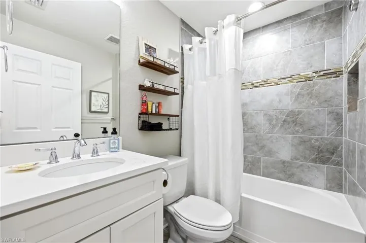 Bathroom featuring a white vanity with an undermount sink and polished chrome faucet, an integrated shower-tub combination, a tiled shower surround with an accent band, and a shower niche