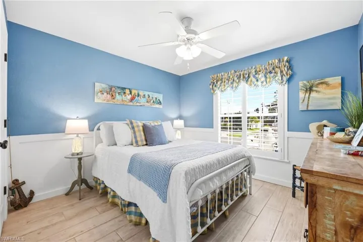 Bedroom featuring light wood-finish flooring, two-tone walls with wainscoting, and a ceiling fan with integrated lighting